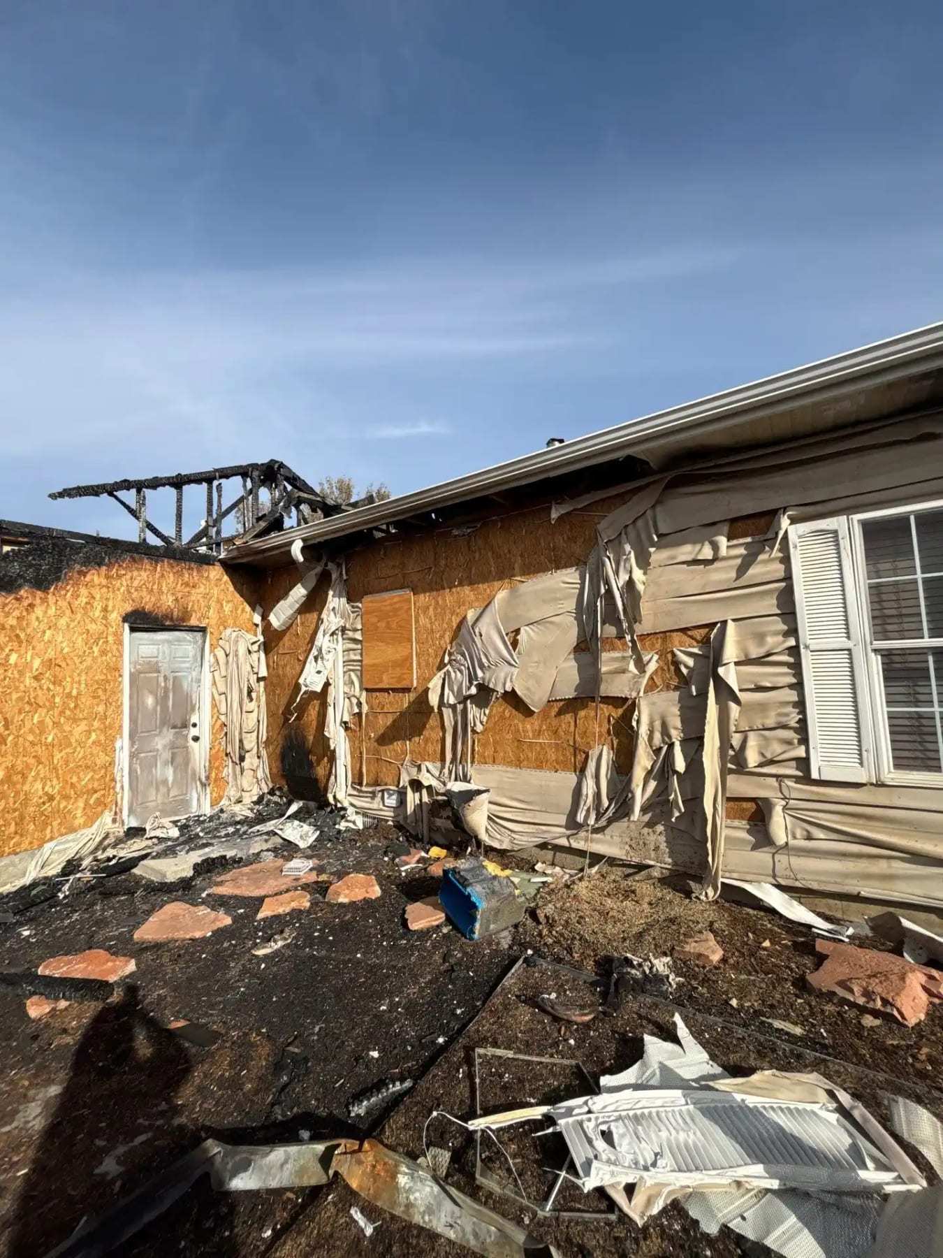 Fire-damaged house exterior with the roof open and debris on the ground