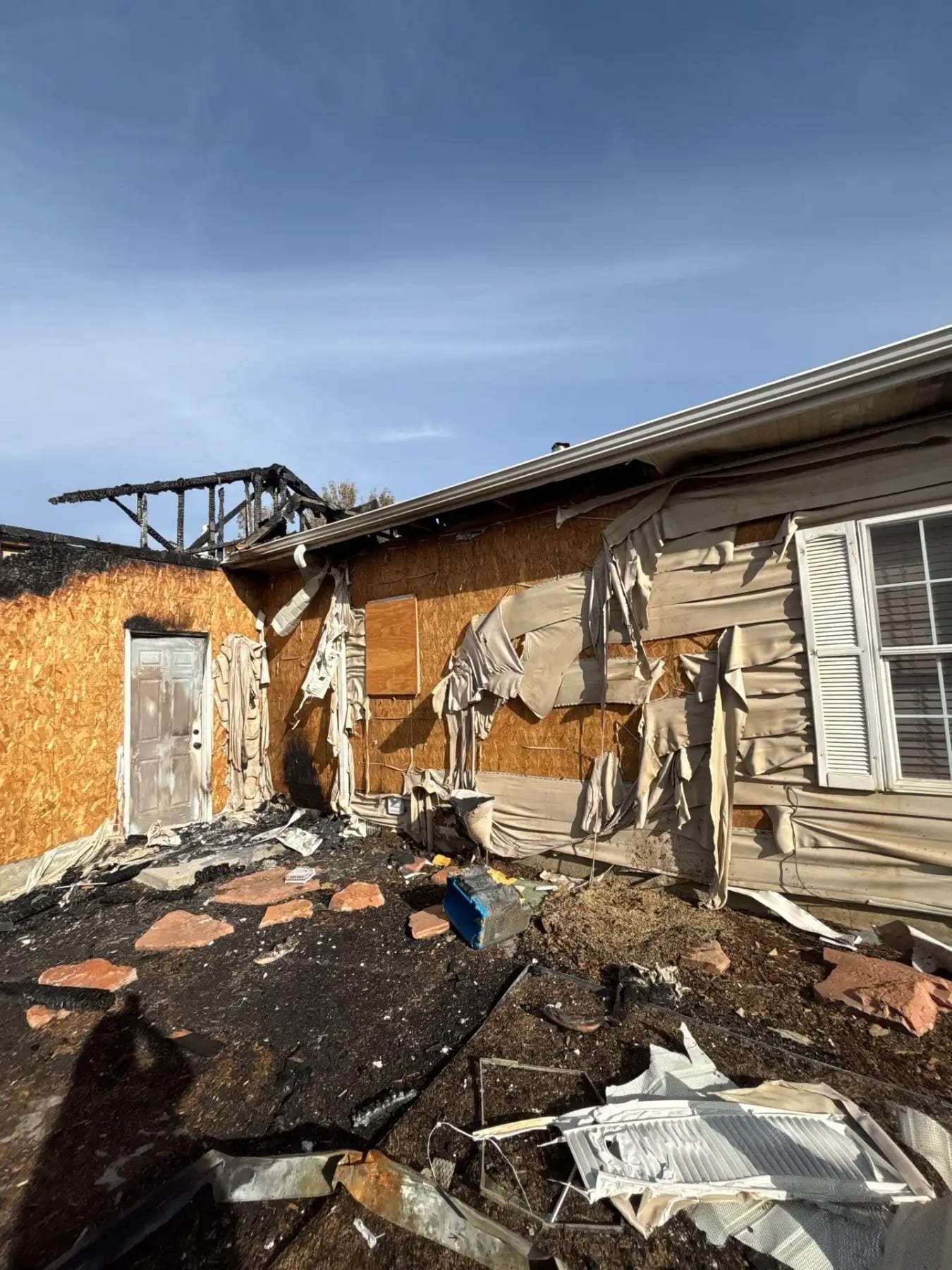Fire-damaged house exterior with the roof open and debris on the ground